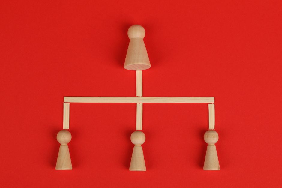 Conceptual depiction of hierarchy using wooden pieces on a vibrant red background.