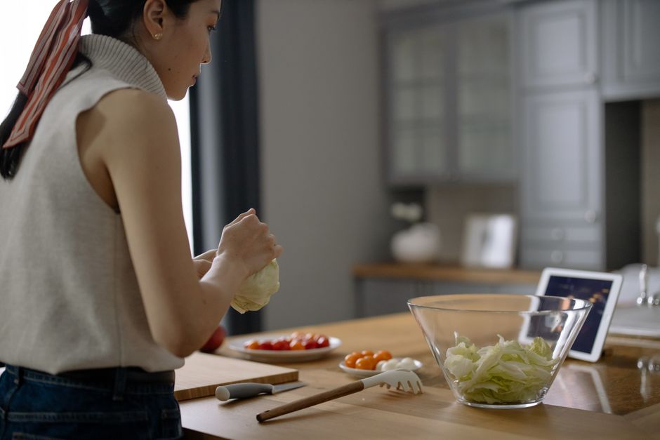 Asian woman preparing a fresh salad with tomatoes and lettuce in a contemporary kitchen setting.