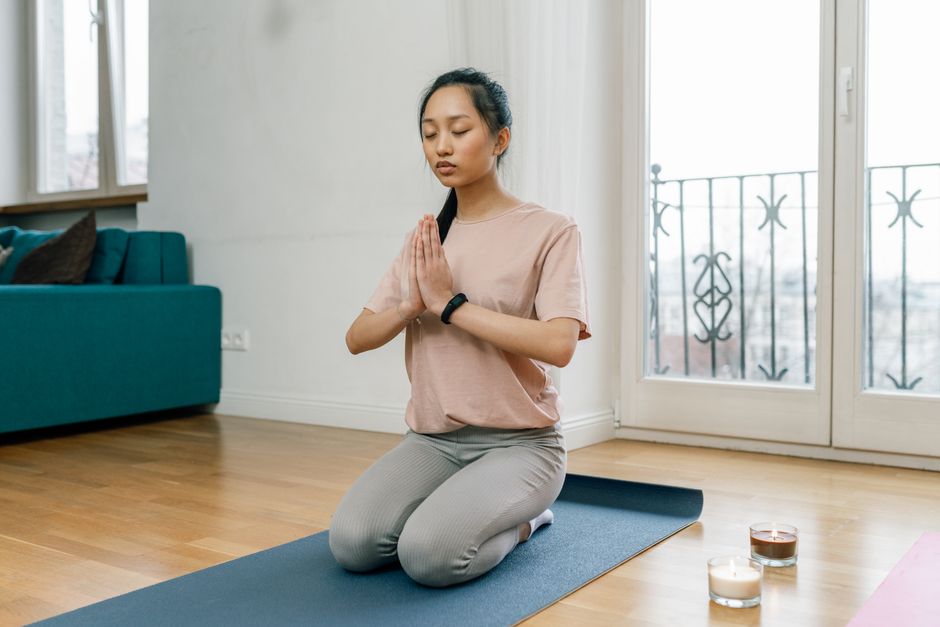 A woman practicing meditation and relaxation indoors on a yoga mat, promoting a healthy lifestyle.