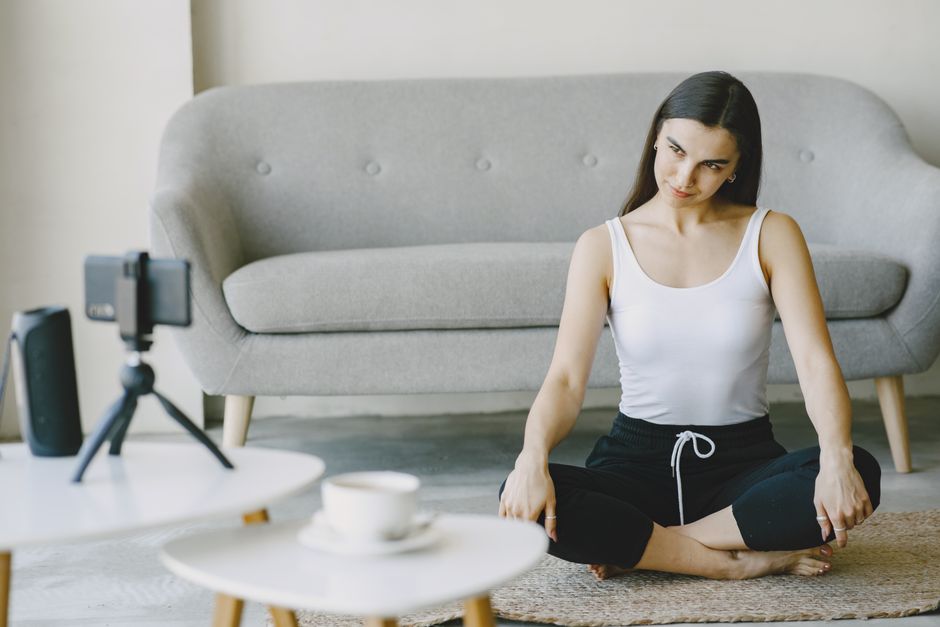 A woman in workout attire doing yoga at home, recording on a smartphone.