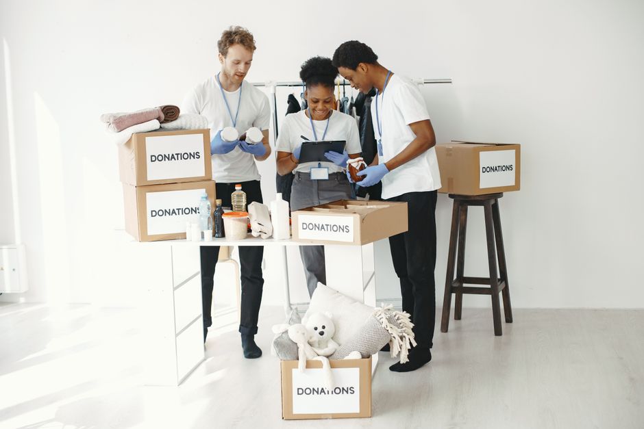 Three volunteers organize donation boxes filled with essentials in a bright indoor setting.