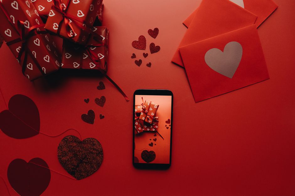 Flat lay of Valentine's Day gifts, envelopes, and phone on a red background with heart motifs.