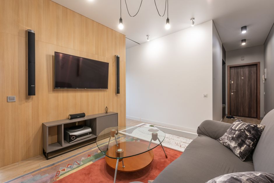 Interior of contemporary light apartment with couch with pillows near table on carpet and cabinet with TV on wall with speakers near lamps on ceiling