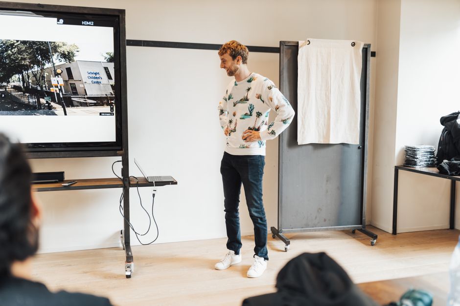 Man presenting on a large screen in a modern office setting, engaging an audience.