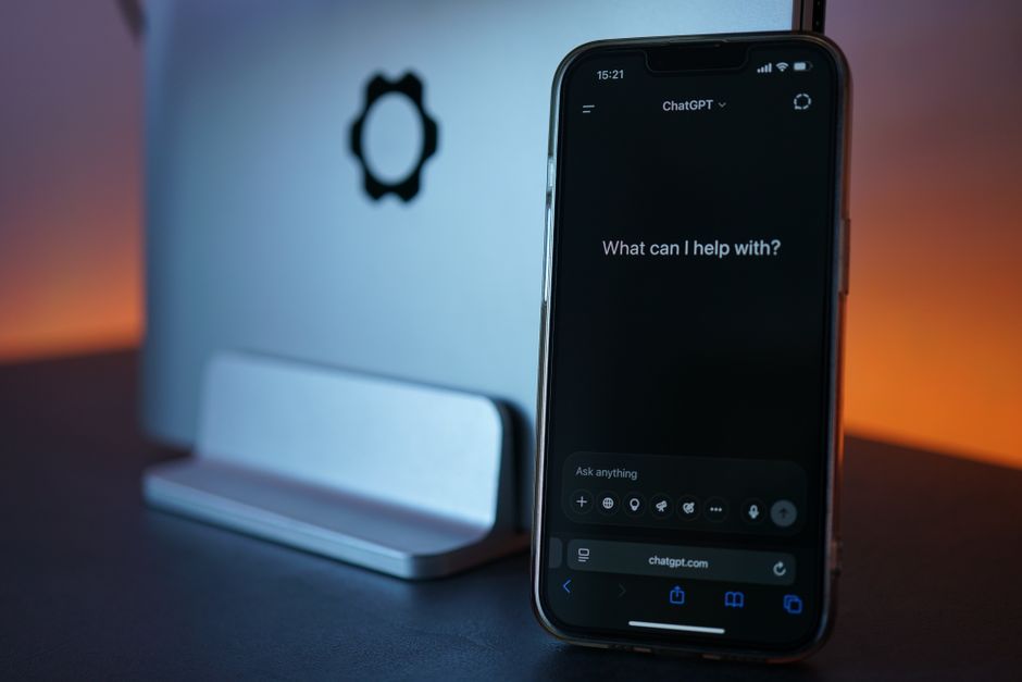Close-up of a smartphone showing a chat interface with a laptop in the background.